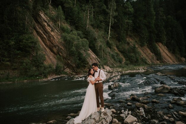 Elegante dolce elegante sposa e sposo in riva al fiume con pietre in montagna Una coppia di sposi amorevole