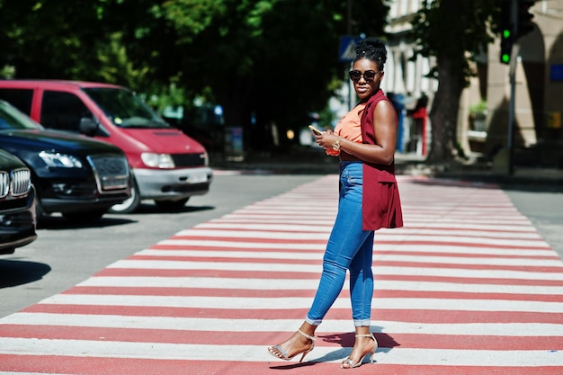 Elegante donna afroamericana che cammina sul passaggio pedonale o pedonale con il telefono cellulare a portata di mano