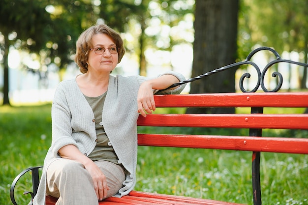 Elegante donna anziana con la maglietta è seduta su una panchina in un parco in una calda giornata