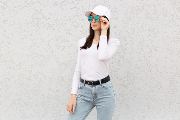 Elegante donna attraente con i capelli scuri in posa vicino al muro bianco e distogliere lo sguardo