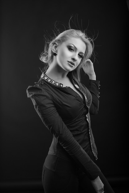 Elegante donna bionda con trucco perfetto e lunghi capelli svolazzanti indossa camicetta, posa in studio. Scatto in bianco e nero