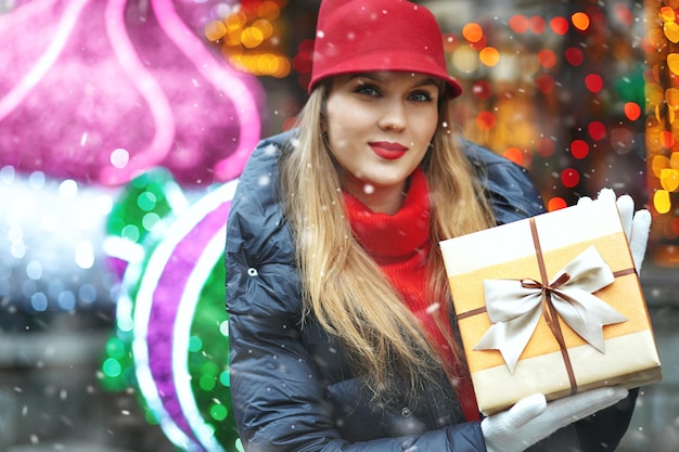 Elegante donna bionda con una confezione regalo al mercatino di Natale di strada durante la nevicata. Spazio vuoto