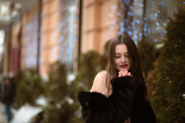 Elegante donna bruna con gli occhi chiusi, con indosso una pelliccia, in posa sullo sfondo del bokeh