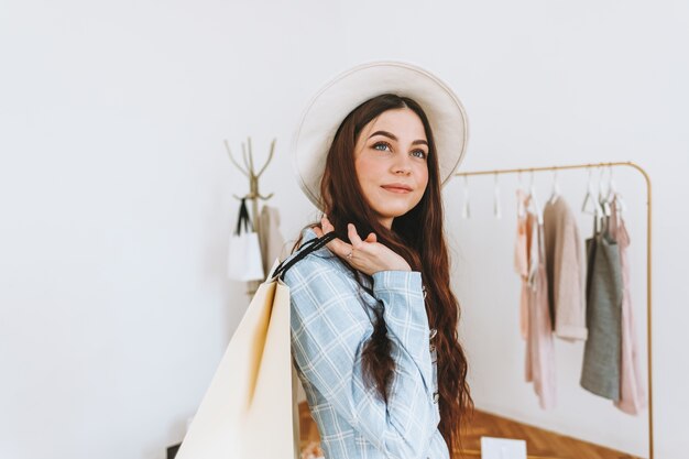 Elegante donna caucasica in cappello e con la borsa della spesa nella boutique di moda