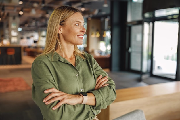 Elegante donna d'affari di mezza età in piedi con le mani incrociate sullo sfondo dello spazio di coworking