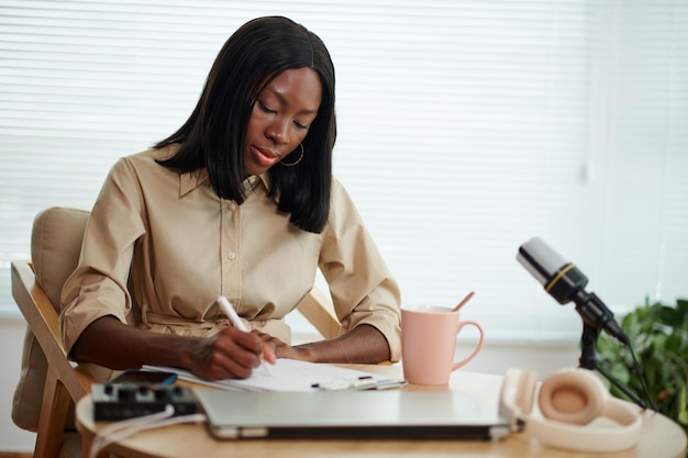 Elegante donna di colore che beve caffè e lavora alla sceneggiatura per il podcast