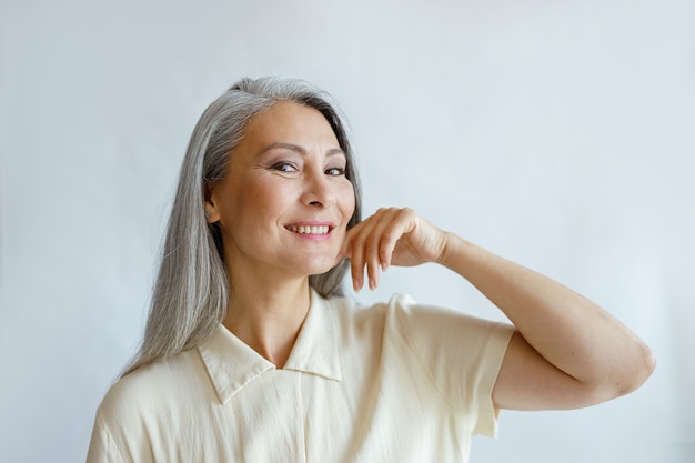 Elegante donna di mezza età con capelli canuti posa su sfondo chiaro