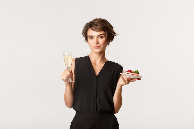 Elegante donna elegante partecipare alla festa, tenendo in mano un bicchiere di champagne e un pezzo di torta