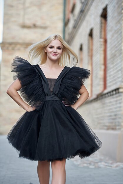 elegante donna felice all'aperto che indossa un abito nero sorridendo alla telecamera