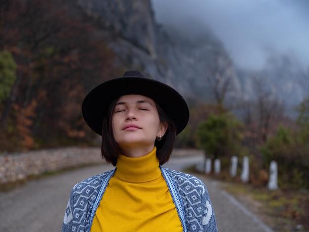 Elegante donna hipster in un cappello che cammina lungo una strada di montagna