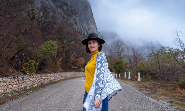 Elegante donna hipster in un cappello che cammina lungo una strada di montagna