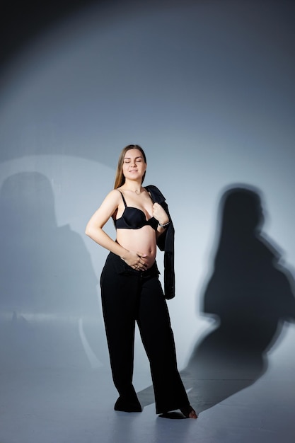 Elegante donna incinta Bella ragazza incinta con i capelli lunghi in abito nero su sfondo grigio concetto di felice gravidanza e famiglia