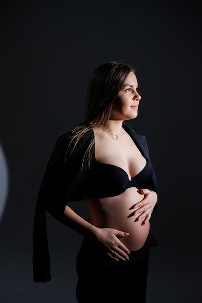 Elegante donna incinta Bella ragazza incinta con i capelli lunghi in abito nero su sfondo grigio concetto di felice gravidanza e famiglia