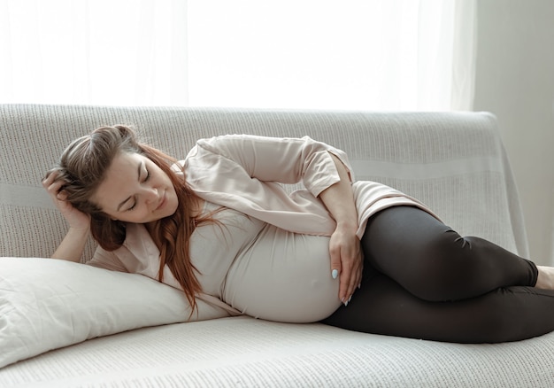 Elegante donna incinta nell'ultimo mese che riposa sul divano di casa.