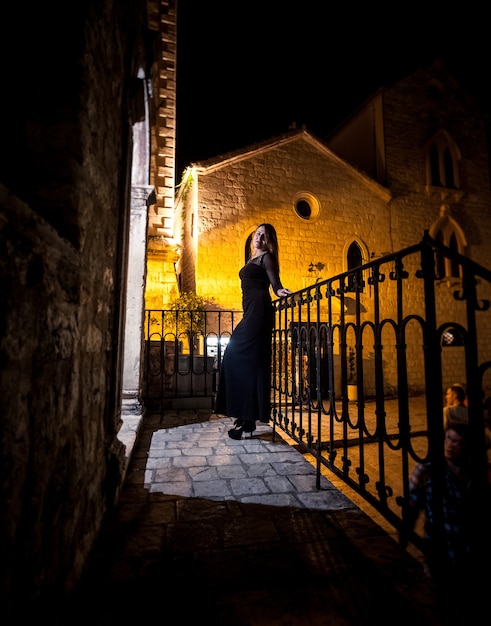 Elegante donna magra in abito da cocktail in posa sulla vecchia strada buia