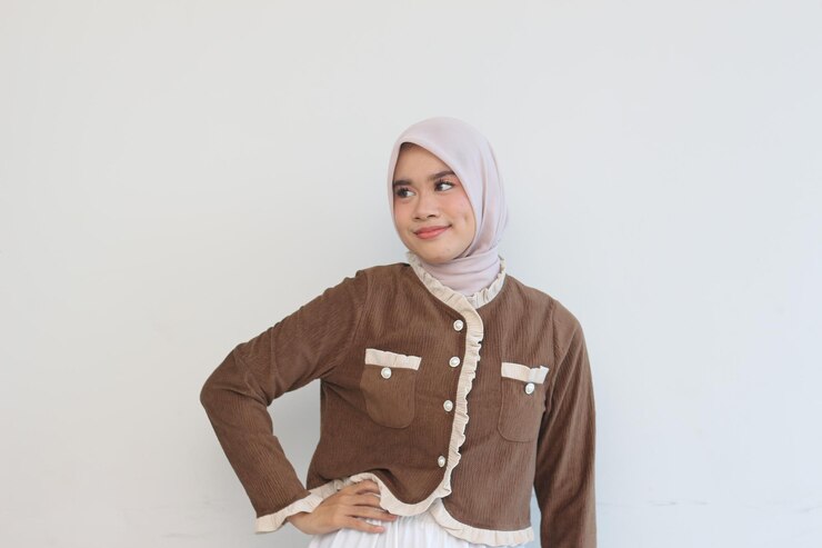 Elegante donna musulmana con giacca di corduroy marrone e hijab beige che posa su uno sfondo bianco