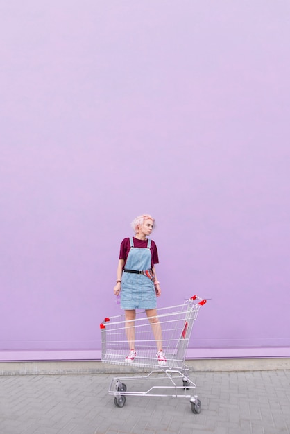 elegante giovane donna con i capelli rosa in piedi in un carrello sullo sfondo di un muro viola