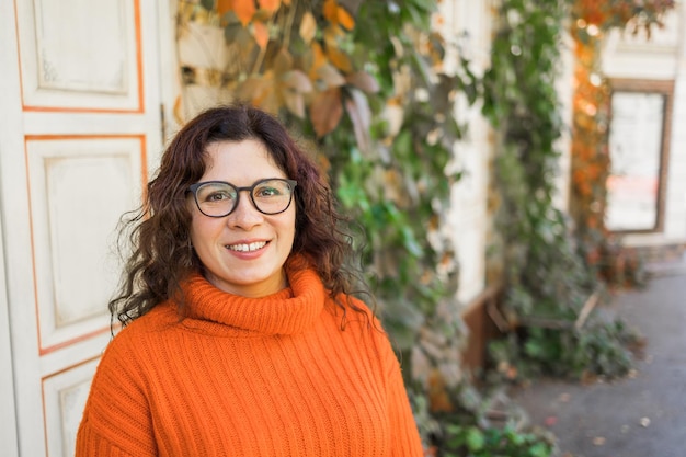 Elegante giovane donna felice che indossa felpa arancione e occhiali da vista Ritratto di ragazza sorridente in occhiali alla moda nello spazio della copia della città e spazio vuoto per la pubblicità