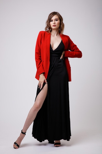 Elegante giovane donna in abito da sera nero con giacca rossa scollo profondo su sfondo bianco