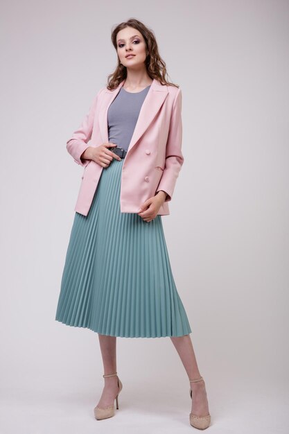 Elegante giovane donna in bel vestito, giacca blazer rosa pallido, gonna verde in posa su sfondo bianco