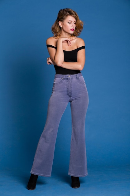 elegante giovane donna in jeans denim, top nero in posa su sfondo blu