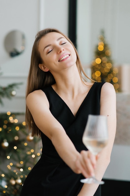 Elegante giovane donna in un abito nero tiene un bicchiere di champagne nelle sue mani e gode di alcol