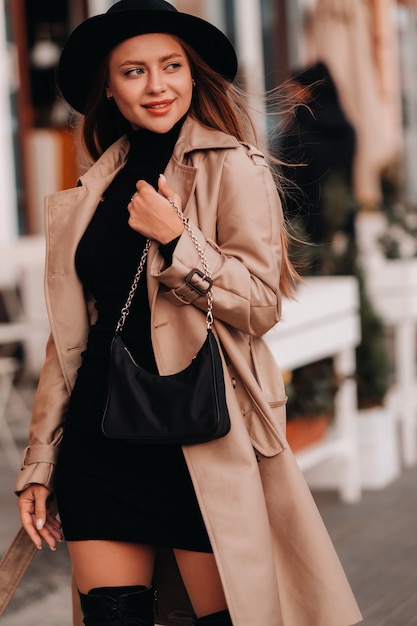 Elegante giovane donna in un cappotto beige e un cappello nero