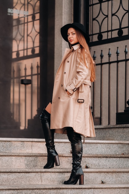 Elegante giovane donna in un cappotto beige in un cappello nero su una strada cittadina. Moda di strada femminile. Abbigliamento autunnale Stile urbano.