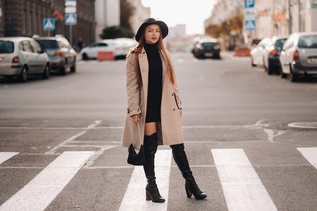 Elegante giovane donna in un cappotto beige in un cappello nero su una strada cittadina. Moda di strada femminile. Abbigliamento autunnale Stile urbano.