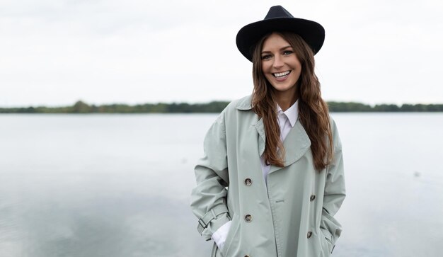 Elegante giovane donna in un cappotto grigio e cappello sullo sfondo del mare