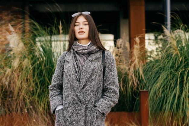 Elegante giovane ragazza bruna in cappotto grigio alla moda in posa per le strade della città