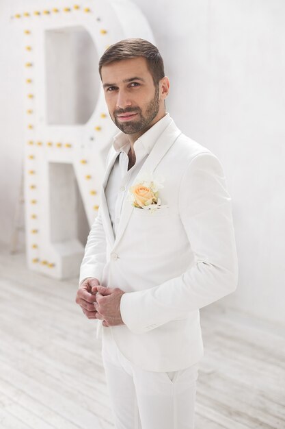 Elegante giovane uomo bello con la barba in un abito classico bianco