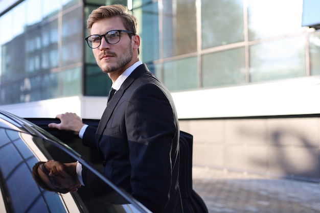 Elegante giovane uomo d'affari che entra nella sua auto mentre si trova all'aperto.