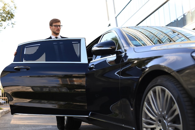 Elegante giovane uomo d'affari che entra nella sua auto mentre si trova all'aperto.