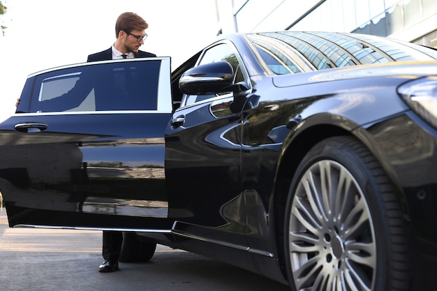 Elegante giovane uomo d'affari che entra nella sua auto mentre si trova all'aperto.