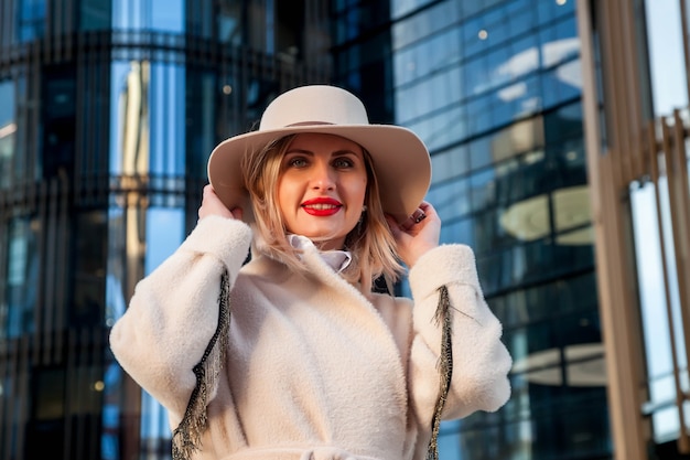 Elegante imprenditrice all'aria aperta contro il business center. Donna in camice bianco e cappello nel quartiere degli affari