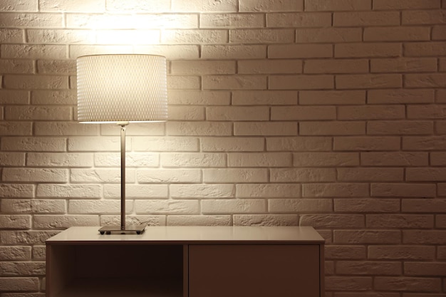 Elegante lampada da notte incandescente sul tavolo vicino al muro di mattoni bianchi Spazio per il testo