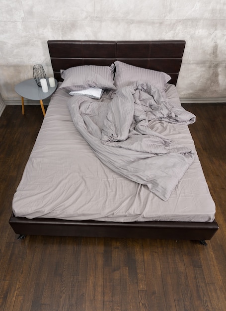 Elegante letto con coperta stropicciata nei colori grigi e comodino con candele