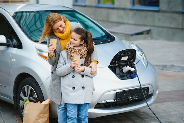 Elegante madre e figlia caricano un'auto elettrica e trascorrono del tempo insieme