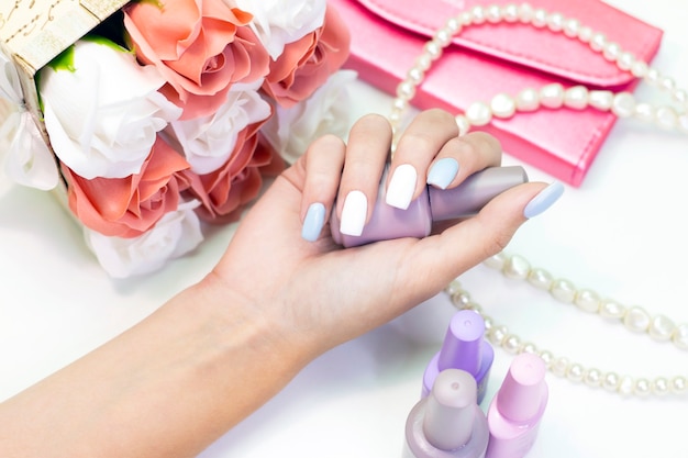 Elegante manicure femminile alla moda. Belle mani di una giovane donna su uno sfondo di fiori e perle di perle