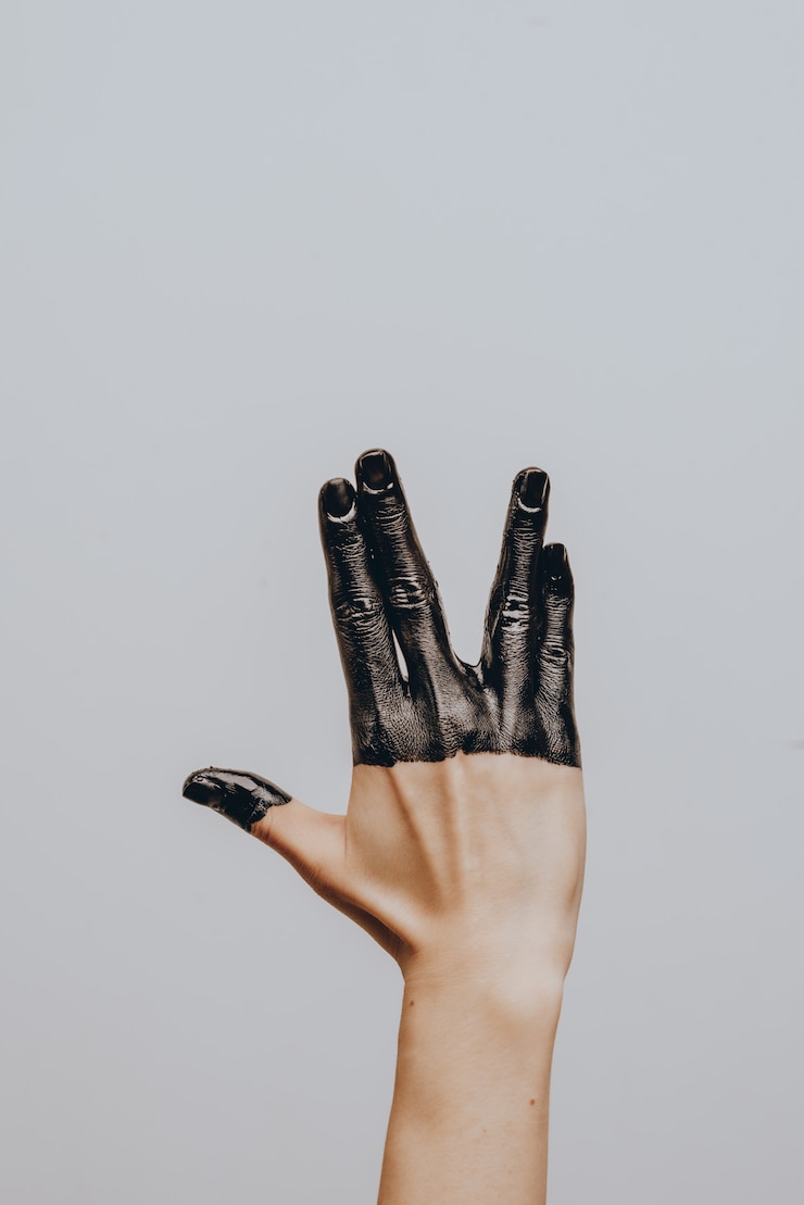 Foto elegante mano femminile immersa in vernice nera. isolato. gesto.