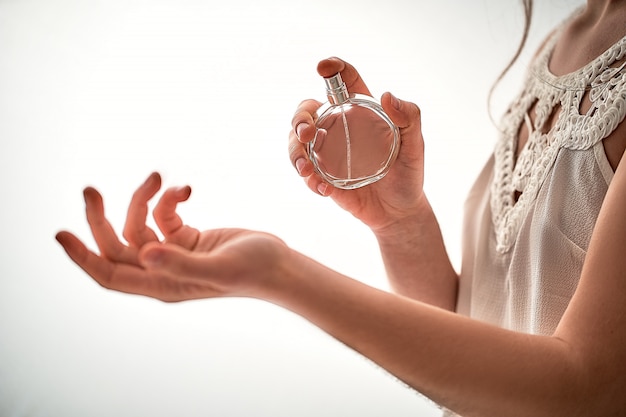 Elegante moda donna alla moda in camicetta bianca applicando sul polso profumo preferito profumo su un muro bianco