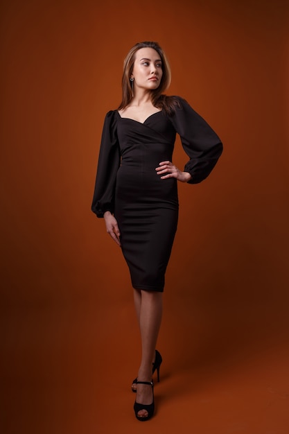 Elegante modella che indossa un abito nero con profonda scollatura in posa su sfondo arancione