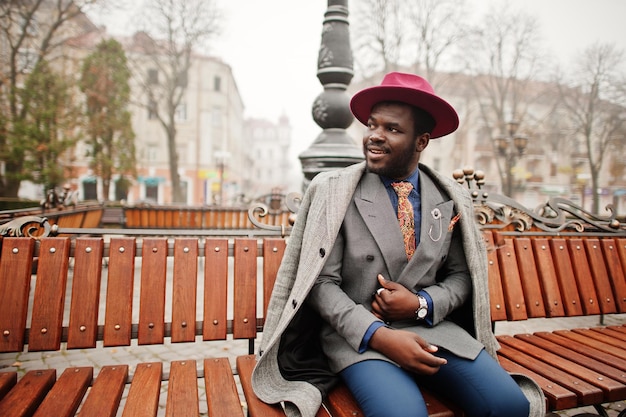 Elegante modello da uomo afroamericano in giacca grigia con cravatta e cappello rosso in posa al banco