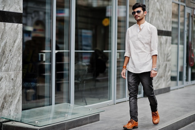 Elegante modello indiano uomo in abiti casual e occhiali da sole poste all'aperto in strada dell'India