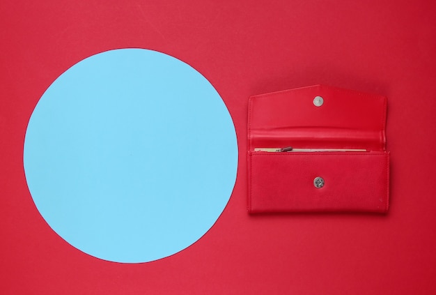 Elegante portafoglio da donna in pelle rossa su sfondo rosso con cerchio blu pastello per lo spazio della copia. Natura morta di moda minimalista creativa. Vista dall'alto