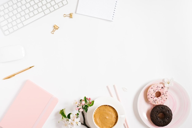 Elegante posto di lavoro piatto per donne con penna per tastiera per notebook e fiori di mela primaverile una tazza di caffè e ciambelle su uno sfondo bianco con spazio per la copia