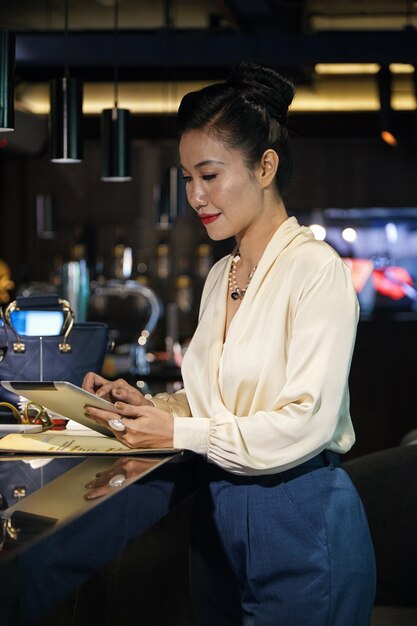 Elegante proprietaria di un ristorante femminile in piedi al bancone del bar e lavorando su un computer tablet