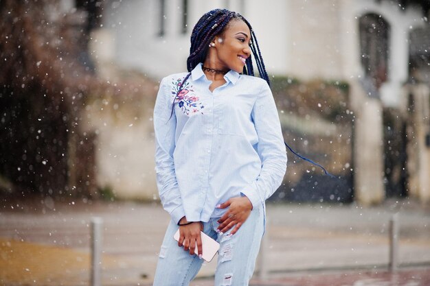 Elegante ragazza afroamericana con dreadlocks che tiene il telefono cellulare a portata di mano all'aperto tempo nevoso