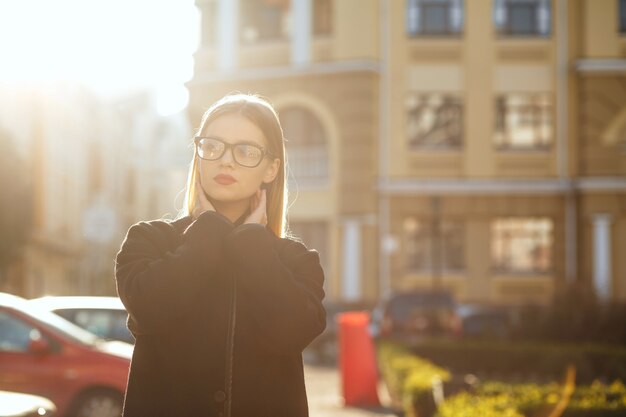 Elegante ragazza bionda con i capelli lunghi che indossa il cappotto, in posa nel bagliore del sole. Spazio per il testo